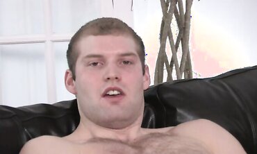 Defined build guy plays with his rod on sectional leather bed.